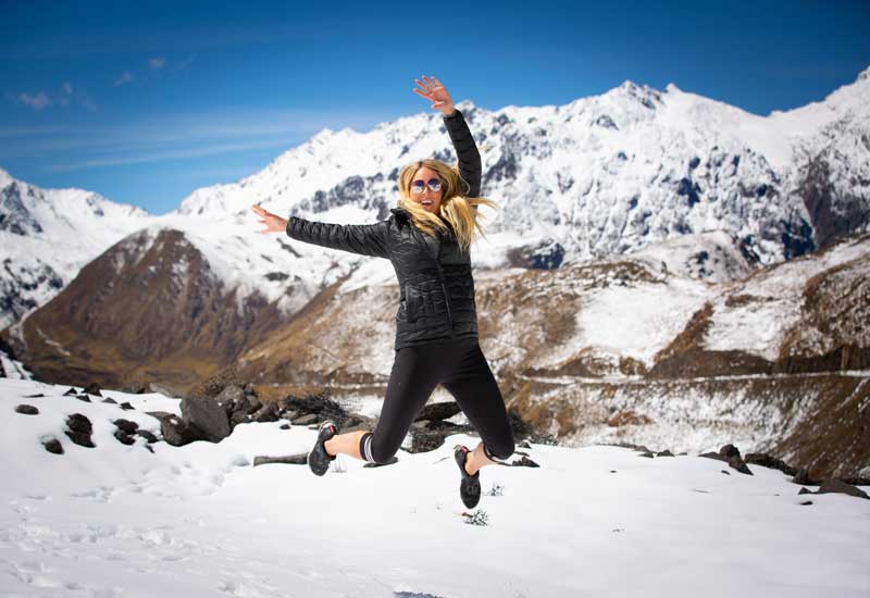 Traveler jumping in the snow at Abra Malaga surrounded by snow-capped Andean mountains in Peru