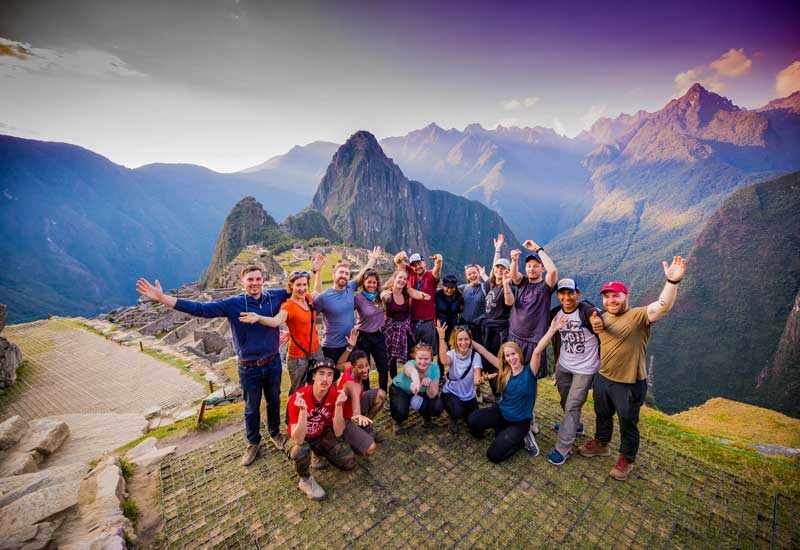 Group of travelers celebrating at Machu Picchu after completing the Inca Trail, with panoramic views of the iconic Inca citadel in Peru