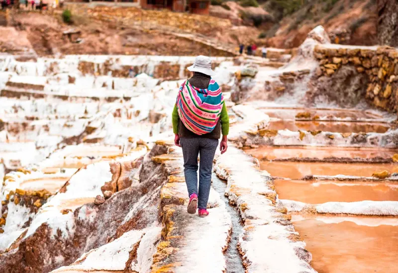 Local woman walking through the Maras Salt Mines surrounded by traditional salt ponds in the Sacred Valley of Peru