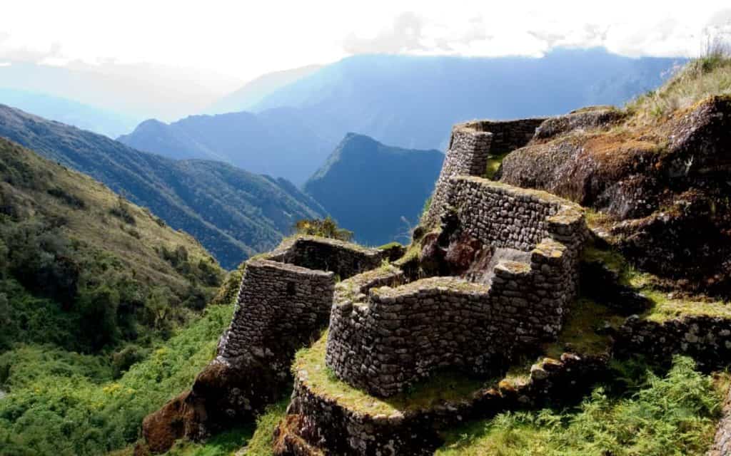 Puyupatamarca archaeological site on the Inca Trail with stone terraces, ceremonial structures, and cloud-covered Andes mountains in Peru