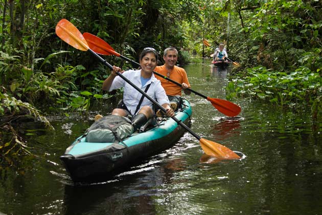 A happy couple kayaking together on a calm Amazon River surrounded by dense rainforest and tropical greenery.