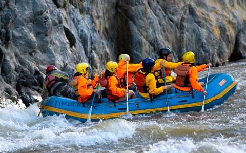 Inca Jungle Pricing Booking, Adventure travelers rafting on a fast-flowing river surrounded by lush green mountains in the Andes of Peru.