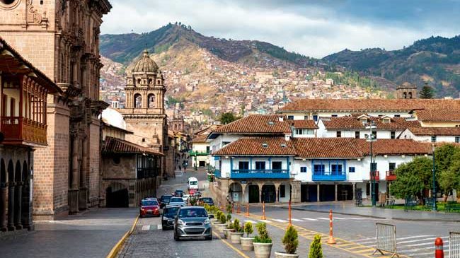 Small square near town in Cusco Peru with stone paving, colonial buildings, local people, and Andean mountain backdrop