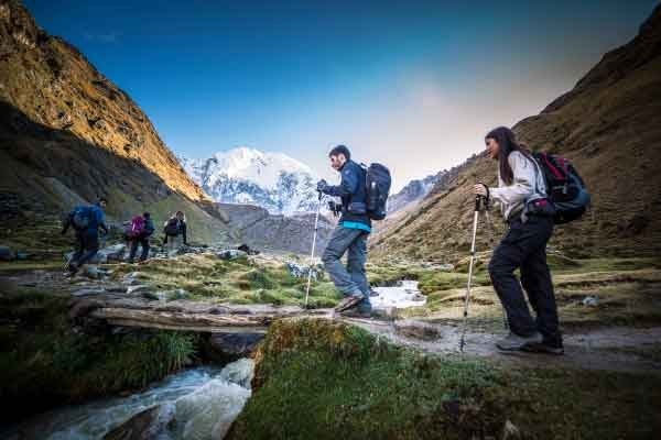 Group of tourists hiking along a mountain trail in the Andes, likely on the Salkantay Trek, surrounded by rugged peaks and high-altitude landscapes.