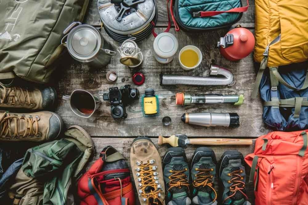 Camping gear arranged outdoors: a tent, backpack, sleeping bag, and cooking equipment ready for an adventure in nature.